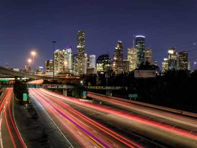 Houston skyline at night with headlights and taillights zooming by